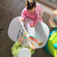 Two children sitting at a small table with coloring books and crayons.